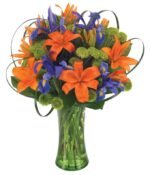 Orange lilies are arranged in a clear glass vase with purple statice and yellow solidago