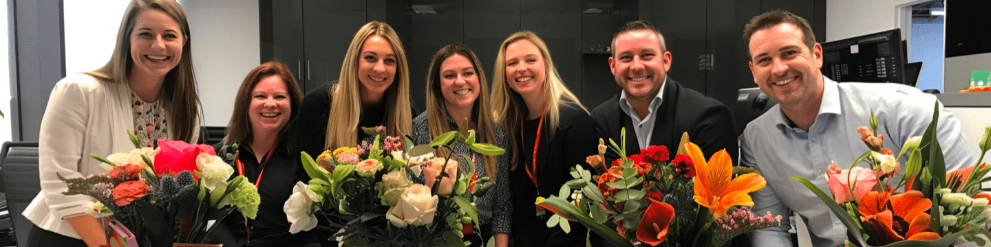 A group of office workers smiling and motivated, surrounded by vibrant bouquets of flowers they've received, boosting their morale and creating a positive work environment